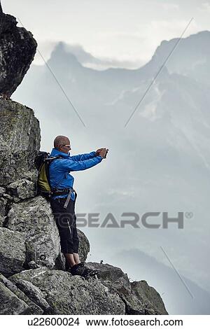 "Mature man on rocks taking photo, Valais, Switzerland" View Large Photo Image Picture - "Mature man on rocks taking photo, Valais, Switzerland". Fotosearch