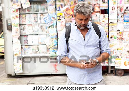 Stock Image - "Mature man reading smartphone texts on street, Copacabana town, Rio De Janeiro, Brazil". Fotosearch