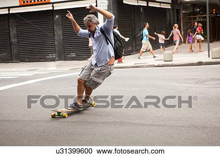 Stock Image - "Mature man skateboarding on road, Copacabana town, Rio De Janeiro, Brazil". Fotosearch