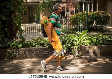 "Mature man strolling on sidewalk carrying skateboard, Rio De Janeiro, Brazil" View Large Photo Image Stock Photograph - "Mature man strolling on sidewalk carrying skateboard, Rio De Janeiro, Brazil". Fotosearch