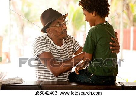 Stock Image - "Mature man talking to grandson sitting on bar, Ipanema beach, Rio De Janeiro, Brazil". Fotosearch