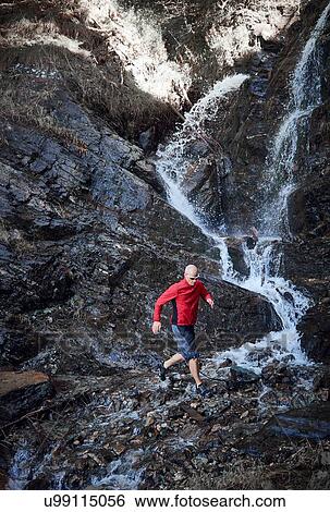 Stock Photograph - "Mature man trail running by waterfall, Valais, Switzerland". Fotosearch