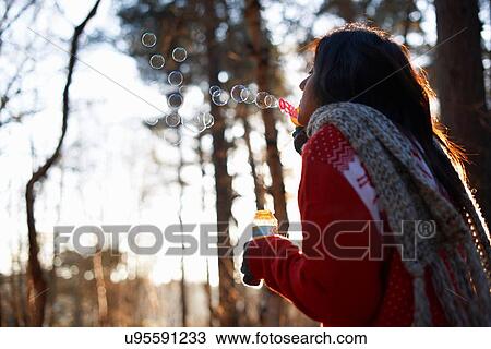 Stock Image - Mature woman blowing bubbles in forest. Fotosearch