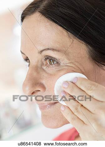 Stock Photo - Mature woman removing make up from face with cotton pad. Fotosearch