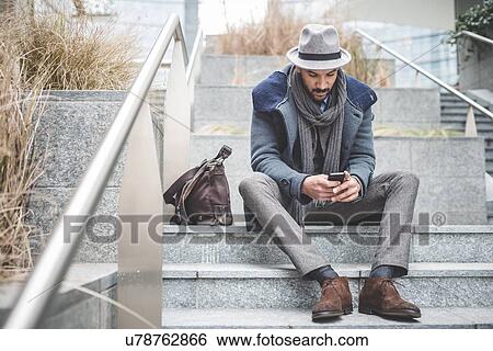 Stock Photograph - Mid adult businessman sitting on stairway reading smartphone text. Fotosearch