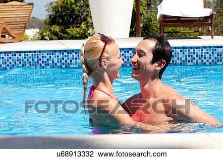 Stock Image - "Mid adult couple in outdoor pool, laughing". Fotosearch