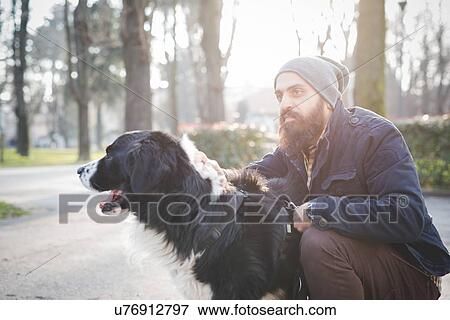 Stock Photo - "Mid adult man, crouching, stroking dog, outdoors". Fotosearch