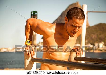 Stock Image - "Mid adult man doing push ups on parallel bars, Rio De Janeiro, Brazil". Fotosearch