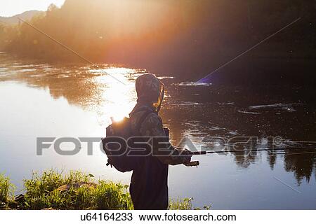 Stock Image - "Mid adult man fishing from riverbank, Sarsy village, Sverdlovsk Region, Russia". Fotosearch