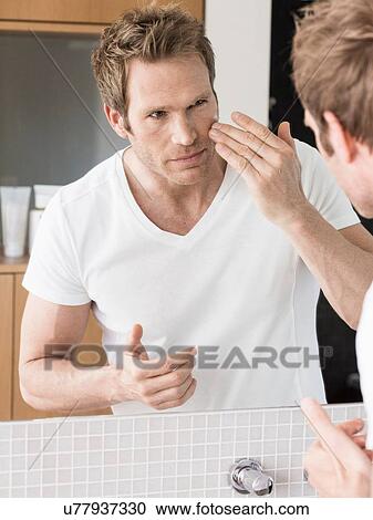 Mid adult man looking in bathroom mirror applying face cream View Large Photo Image Stock Image - Mid adult man looking in bathroom mirror applying face cream. Fotosearch
