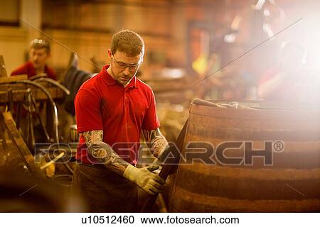 Stock Image - Mid adult man making whisky cask at cooperage. Fotosearch