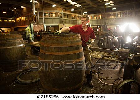 Stock Photograph - Mid adult man making whisky cask at cooperage. Fotosearch