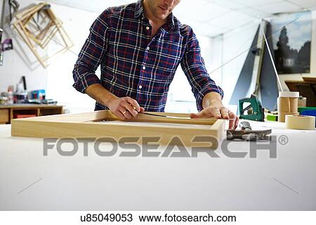 Stock Image - Mid adult man measuring frame on workbench in picture framers workshop. Fotosearch