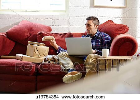 Picture - Mid adult man preparing parcels on sofa in picture framers showroom. Fotosearch