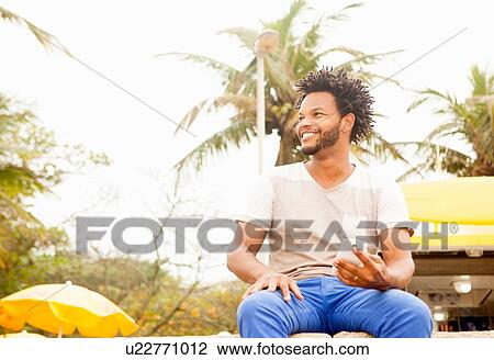 "Mid adult man sitting on wall using smartphone, Ipanema beach, Rio De Janeiro, Brazil" View Large Photo Image Stock Image - "Mid adult man sitting on wall using smartphone, Ipanema beach, Rio De Janeiro, Brazil". Fotosearch