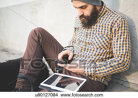 "Mid adult man sitting outdoors with dog, using smartphone and digital tablet" View Large Photo Image Picture - "Mid adult man sitting outdoors with dog, using smartphone and digital tablet". Fotosearch