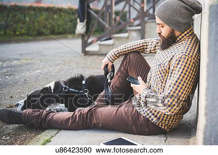 "Mid adult man sitting outdoors with dog, using smartphone" View Large Photo Image Stock Image - "Mid adult man sitting outdoors with dog, using smartphone". Fotosearch