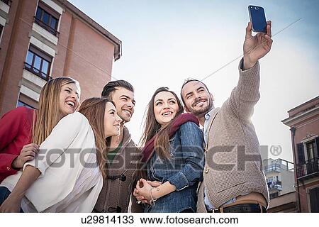 Stock Image - "Mid adult man taking smartphone selfie with friends on street, Cagliari, Sardinia, Italy". Fotosearch