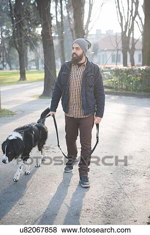 Stock Photo - Mid adult man walking dog through park. Fotosearch