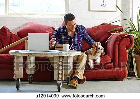 Stock Photo - Mid adult man writing address on parcels whilst petting dog in picture framers. Fotosearch