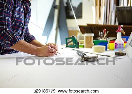 Stock Photo - Mid adult man writing measurement on workbench in picture framers workshop. Fotosearch