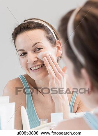 Stock Photo - Mid adult woman looking in mirror cleansing face. Fotosearch