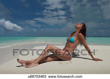 Stock Image - "Mid adult woman sitting on beach, Ari Atoll, Maldives". Fotosearch
