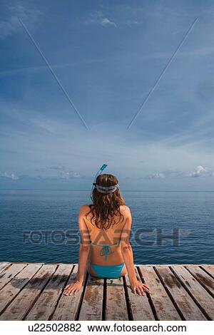 Stock Image - Mid adult woman sitting on pier looking at sea. Fotosearch