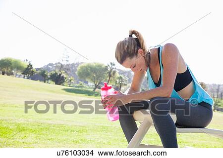 Picture - Mid adult woman training in park drinking water bottle. Fotosearch
