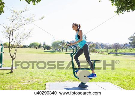 Mid adult woman training on exercise bike in park View Large Photo Image Stock Image - Mid adult woman training on exercise bike in park. Fotosearch