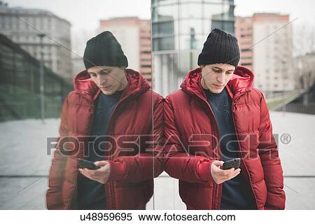 Mirror image of young man leaning against office building reading smartphone texts View Large Photo Image Stock Photography - Mirror image of young man leaning against office building reading smartphone texts. Fotosearch