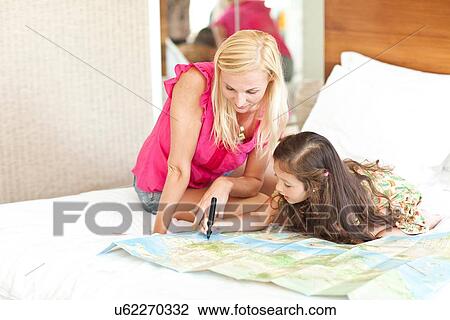 Stock Image - "Mother and daughter lying on bed, looking at map". Fotosearch