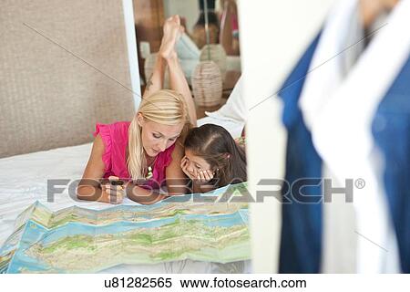 Stock Photography - "Mother and daughter lying on bed, looking at map". Fotosearch