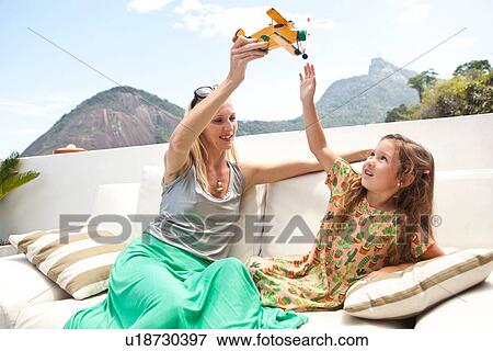 Stock Photo - "Mother and daughter sitting outdoors, playing with toy plane". Fotosearch