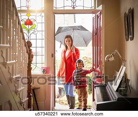 Stock Image - "Mother and son arriving at front door of home on rainy day, portrait". Fotosearch