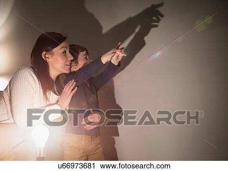 Stock Image - Mother and son making animal shadows on wall. Fotosearch