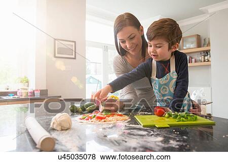 Stock Photo - Mother and son preparing pizza together in kitchen. Fotosearch