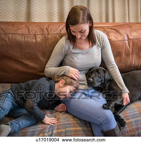 Picture - Mother and son relaxing on sofa at home with pet labrador. Fotosearch