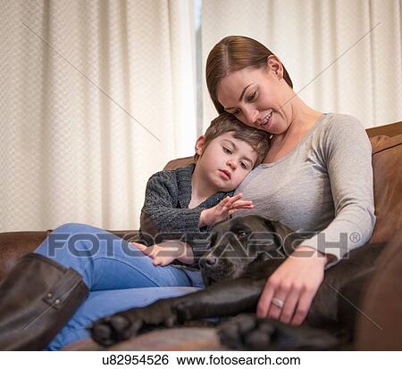 Stock Photograph - Mother and son relaxing on sofa at home with pet labrador. Fotosearch
