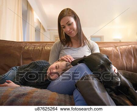 Picture - Mother and tired son relaxing on sofa at home with pet labrador. Fotosearch