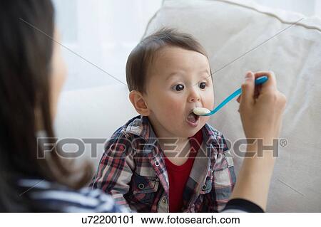 Mother feeding baby boy with spoon View Large Photo Image Stock Image - Mother feeding baby boy with spoon. Fotosearch