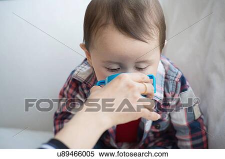 Stock Photography - Mother helping baby boy drink from cup. Fotosearch