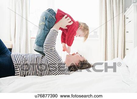 Mother lying on bed lifting son above head View Large Photo Image Stock Image - Mother lying on bed lifting son above head. Fotosearch