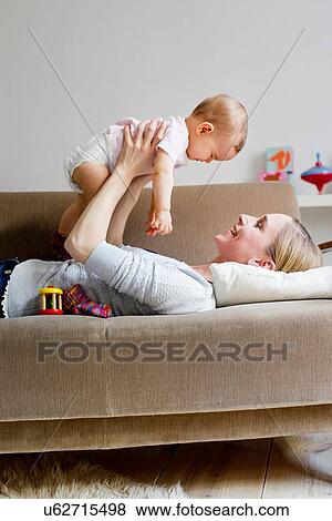 "Mother lying on sofa, holding baby girl in air" View Large Photo Image Stock Photo - "Mother lying on sofa, holding baby girl in air". Fotosearch