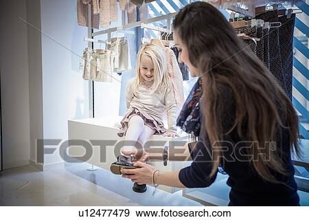 Mother trying shoes on young daughter in childrens clothes shop View Large Photo Image Stock Photo - Mother trying shoes on young daughter in childrens clothes shop. Fotosearch