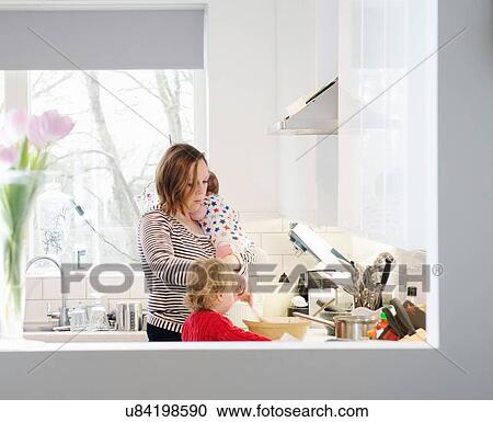 Stock Image - Mother with baby and toddler in kitchen. Fotosearch