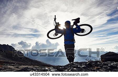 Picture - "Mountain biker carrying bike, Valais, Switzerland". Fotosearch