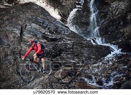 Stock Image - Mountain biker cycling over rocks. Fotosearch
