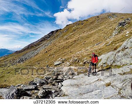 Stock Photography - "Mountain biker pushing bike over rocks, Valais, Switzerland". Fotosearch