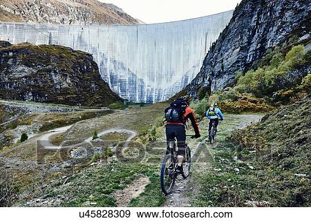 Stock Photo - "Mountain bikers by dam, Valais, Switzerland". Fotosearch